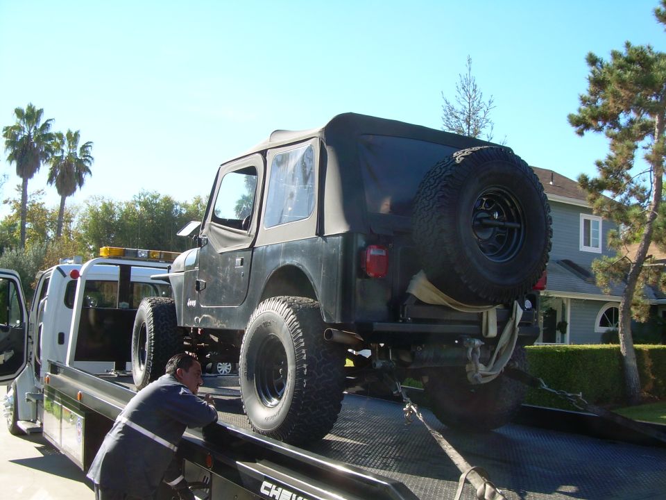 Jeep Wrangler being loaded onto a tow truck with a man in a reflective jacket.
