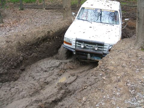 1992 Ford F-350 - A white 1992 Ford F-350 navigates a challenging muddy terrain, with water splashing from its tires.