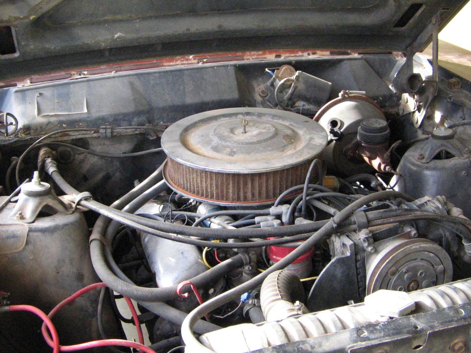 Engine bay with round air cleaner on a V8, wiring, hoses, and brake booster in an older vehicle