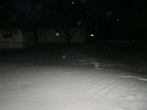 1990 Ford Bronco - A dark, snowy scene at night with a house and trees visible in the background. The foreground is covered in snow with visible ripples from…