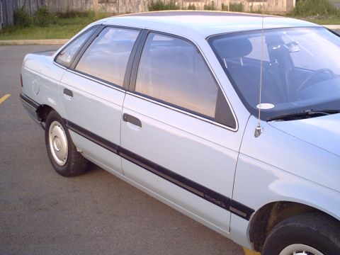 1986 Ford Taurus - The side profile of a light blue sedan is captured in this outdoor photograph.