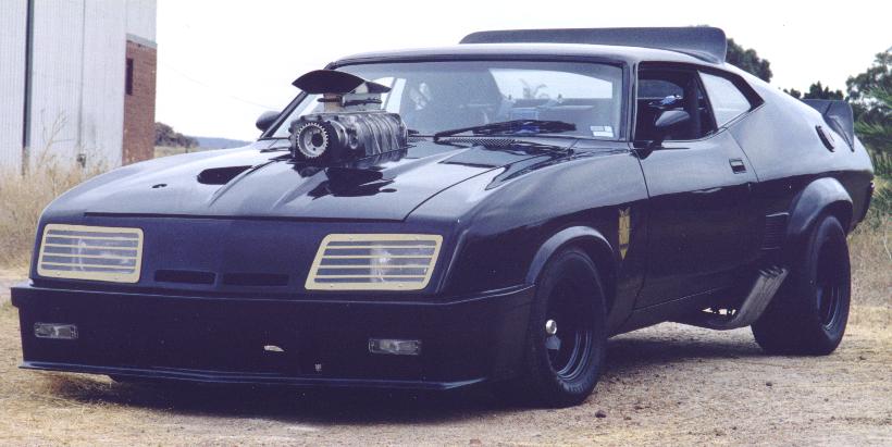 Black modified coupe with supercharger on hood, parked outdoors.