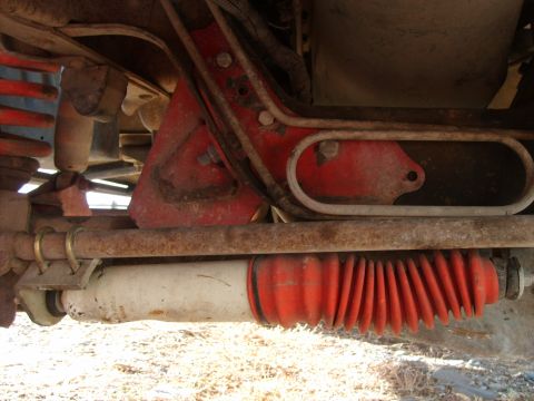 1989 Ford Bronco - The underside of a vehicle shows a red shock absorber boot and a white shock absorber mounted to a rusty metal bar. A red painted bracket i…