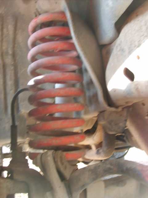 1989 Ford Bronco - A close-up view of the red coil spring suspension system on a 1989 Ford Bronco. The spring is mounted to the vehicle's frame and appears to…