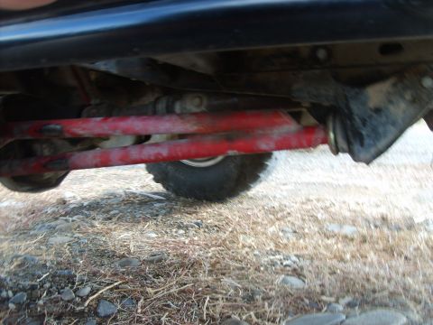 1989 Ford Bronco - The underside of a vehicle shows red-painted suspension components, likely control arms, attached to a black frame. A tire is visible to th…