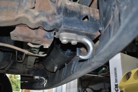 1996 Ford Bronco - A close-up, low-angle view of the undercarriage of a vehicle, showing rusty metal components, a black air tank, and a silver tow hook attac…