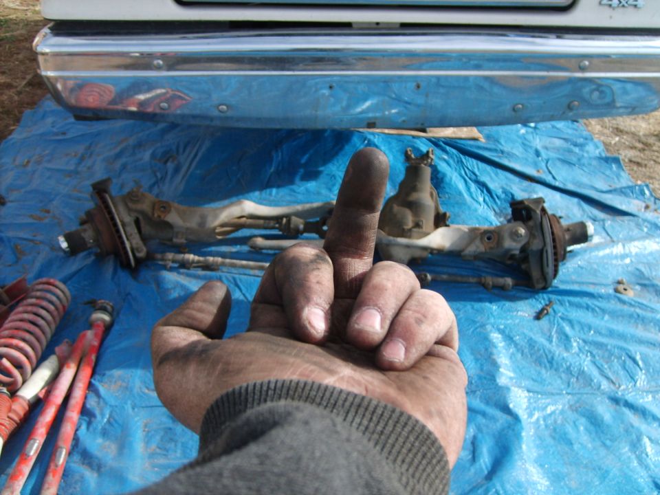 Hand pointing at suspension and steering parts laid on a blue tarp