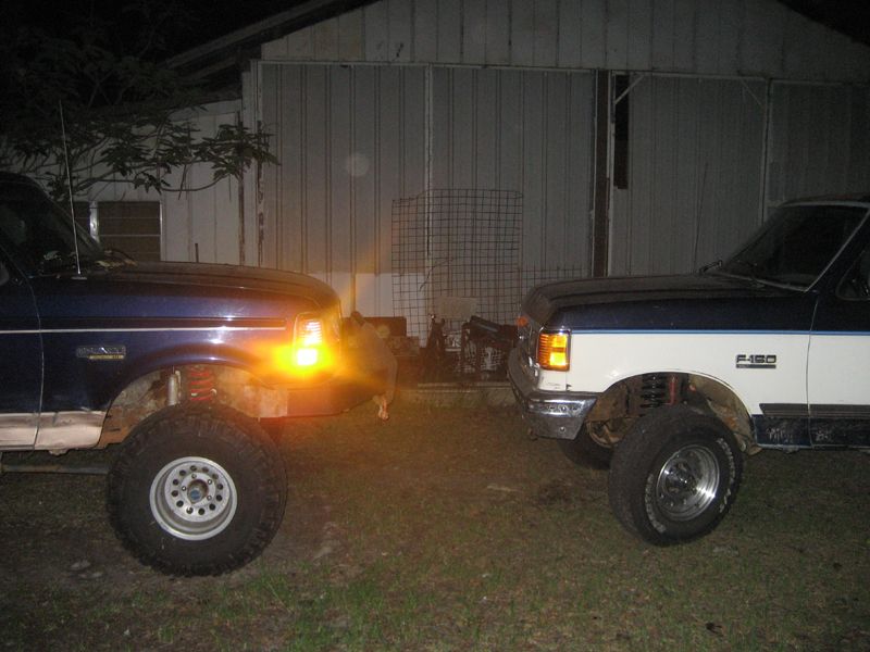 Two lifted Ford F-Series trucks facing each other at night, one with its turn signal on.