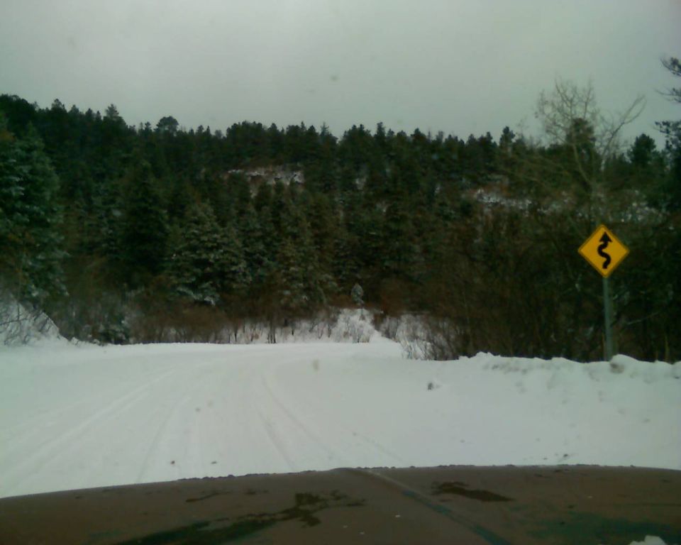 Snowy road through a forest with a curve warning sign.