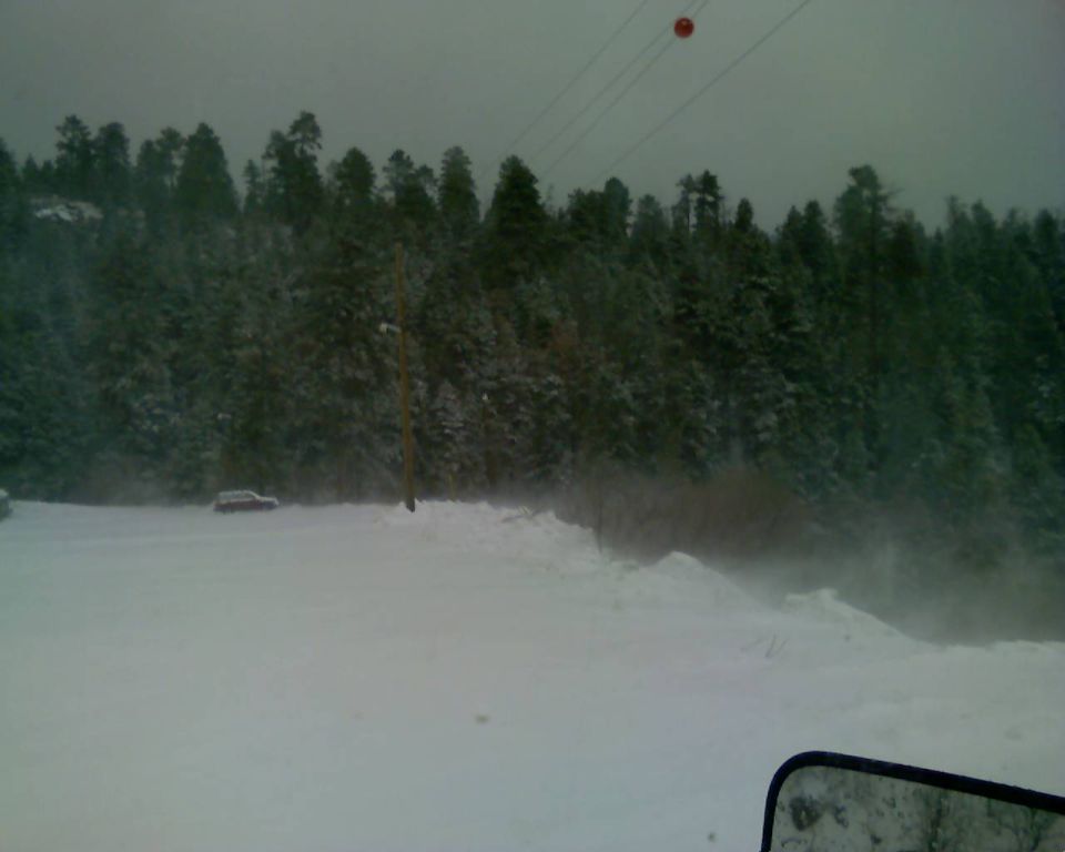 Red car parked in snow with forest behind it.