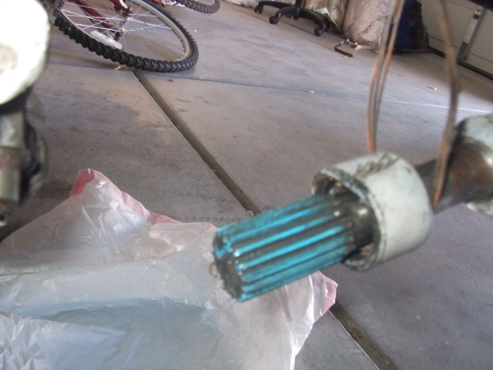 Splined shaft with blue coating and metal boot on a concrete floor next to a plastic bag.