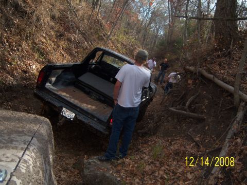 1996 Ford Bronco - A black pickup truck is stuck in a muddy ditch on a wooded trail. Several people are standing around the truck, seemingly assessing the sit…