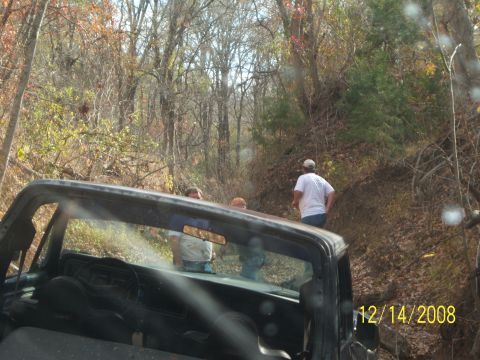 1996 Ford Bronco - A black 1996 Ford Bronco is seen from the interior, looking out through the windshield and side window at a wooded hillside. Two people are…