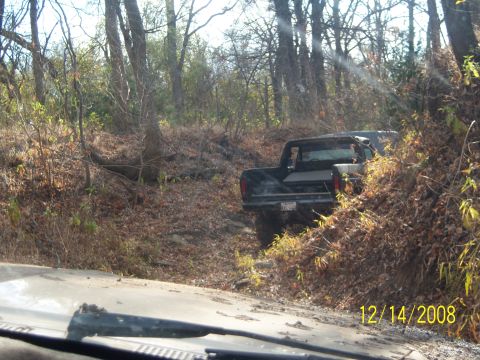 1996 Ford Bronco - A black pickup truck is driving off-road through a wooded area covered in fallen leaves. The truck is angled to the right, with its rear fa…