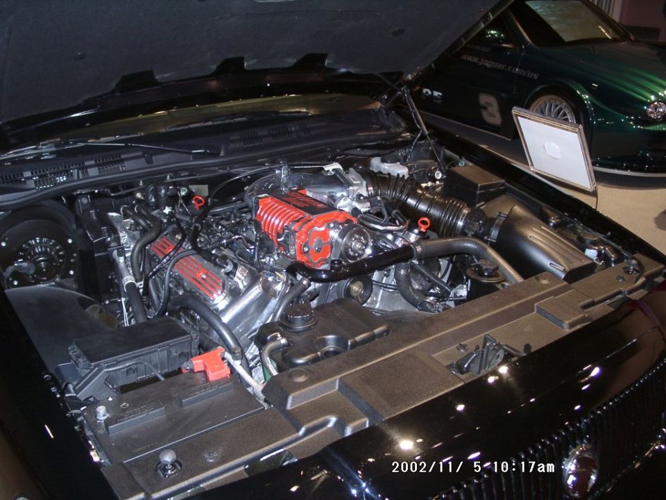 Engine bay with red-topped supercharger on a V8 in a black sedan, indoor display