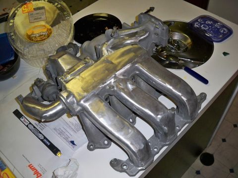 1995 Ford Probe - A polished aluminum intake manifold is laid out on a white surface next to a clear plastic pie container and other miscellaneous items.
