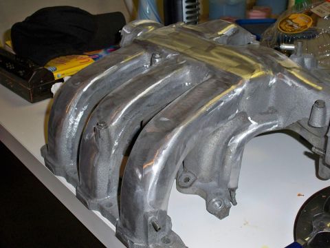 1995 Ford Probe - A close-up, angled view of a polished aluminum intake manifold with visible weld marks. The part is resting on a white surface with other i…
