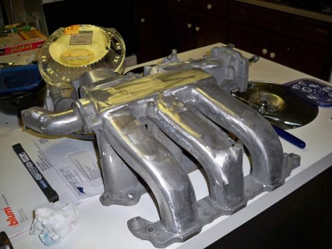 1995 Ford Probe - A polished aluminum intake manifold with four runners is displayed on a table, alongside other automotive parts and documents.