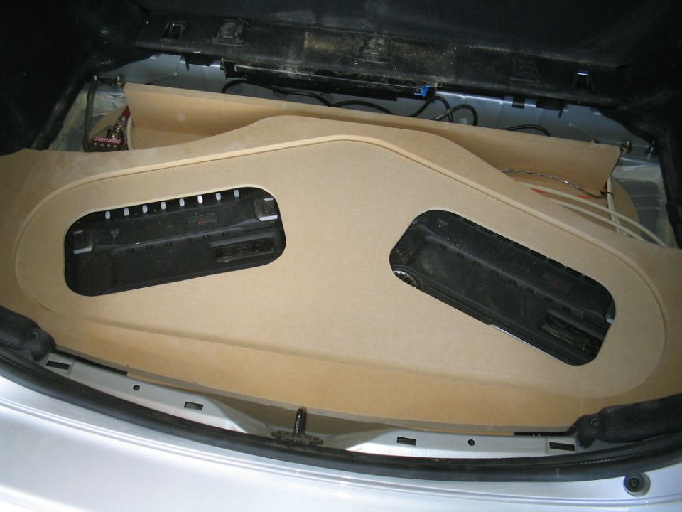 Raw MDF amp rack with two black amplifiers recessed in a car hatch area