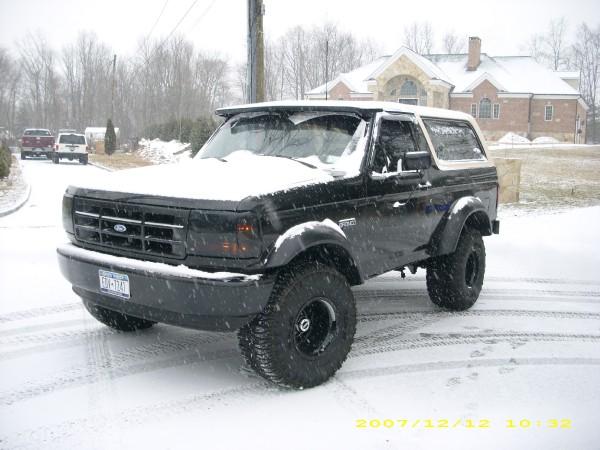 Black Ford Bronco with snow on its roof and hood, parked on a snowy road