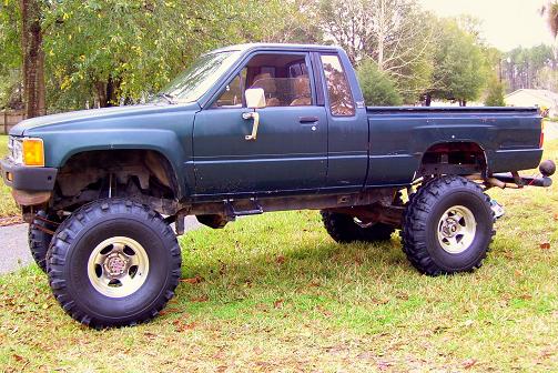 Green lifted Toyota pickup truck, side view. Modified suspension and large tires