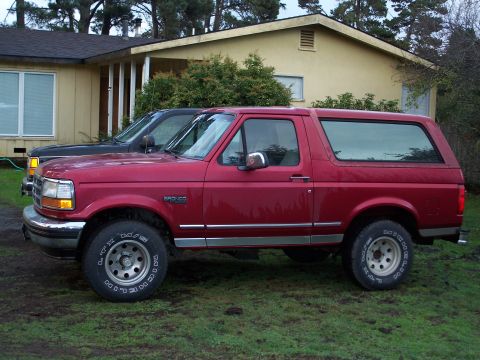 1977 Ford F-150 - A red Ford Bronco is parked in front of a house, with another vehicle partially visible behind it.