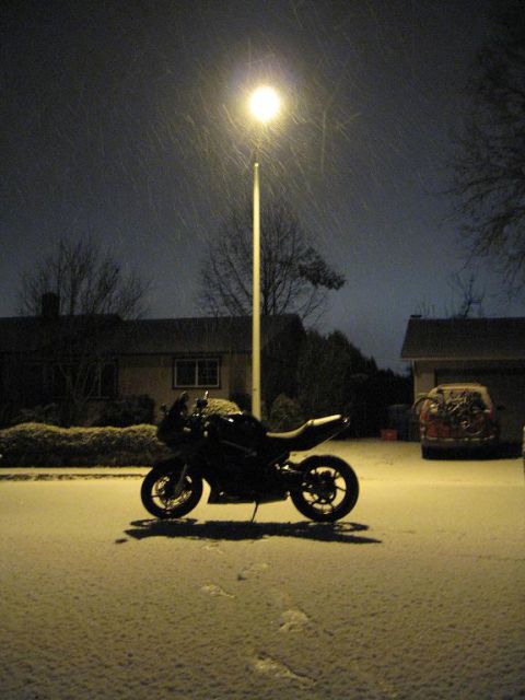 2008 Kawasaki Ninja R - A black motorcycle is parked on a snow-covered street at night, illuminated by a nearby streetlight.