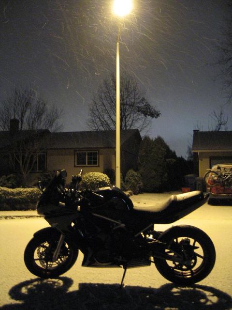 2008 Kawasaki Ninja R - A motorcycle sits parked on a snowy street under a bright street lamp as snow falls.