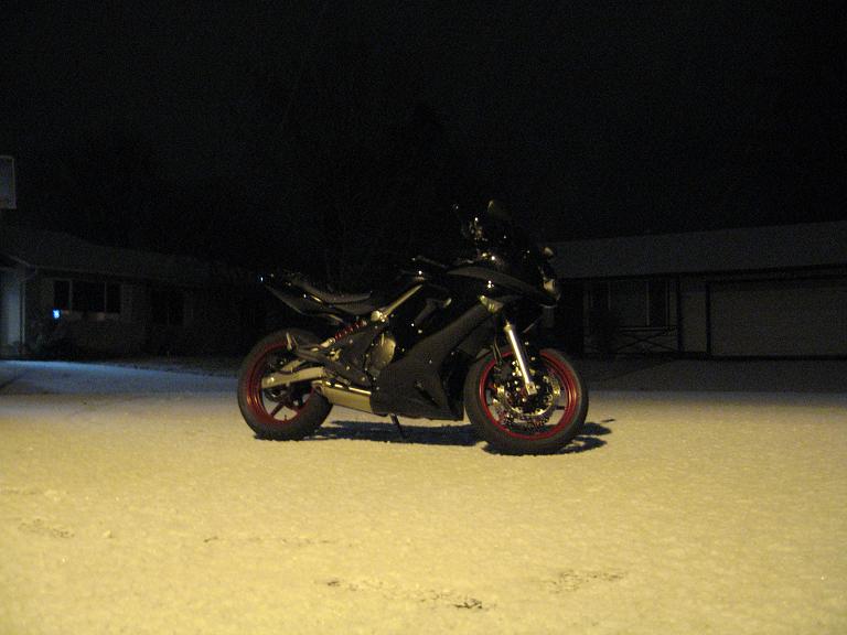 Black motorcycle with red rims parked in snow at night
