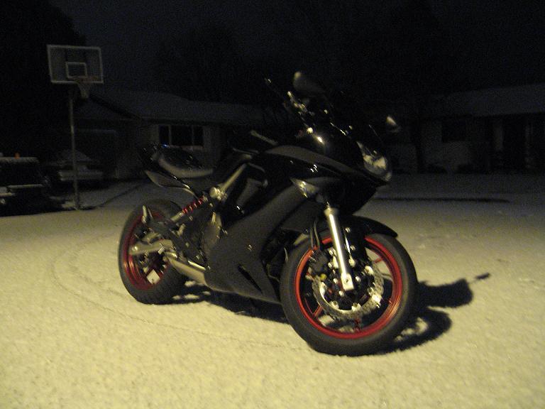 Black motorcycle with red rims parked in snow at night