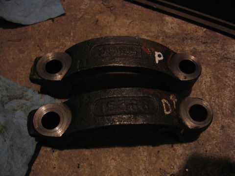 1989 Ford Bronco - Two engine bearing caps with stamped numbers and markings are laid out on a concrete surface.