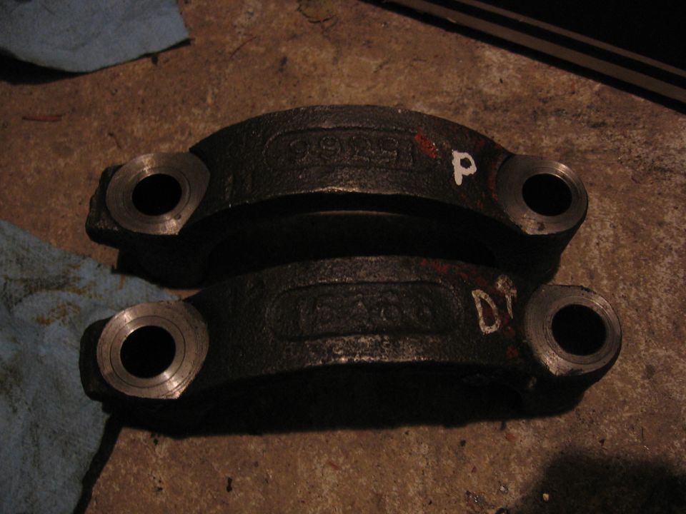 Two black metal engine bearing caps with visible stamped numbers and white markings