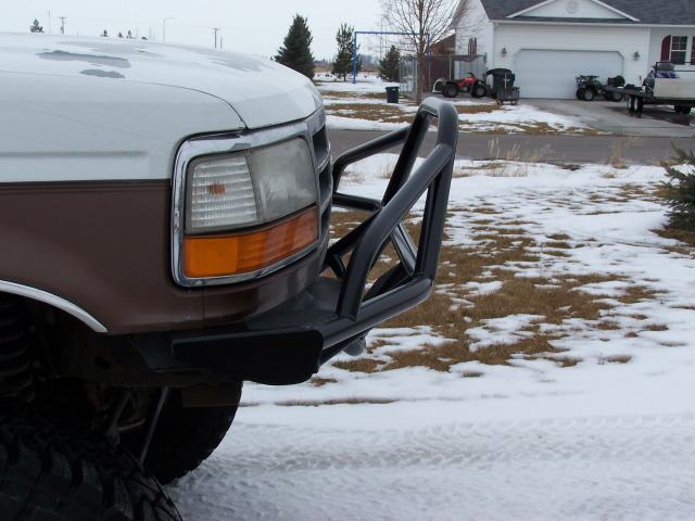 Brown and white Ford truck front bumper with black brush guard, snow on ground