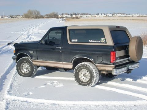 1996 Ford Bronco - A two-tone Ford Bronco navigates a snowy landscape with tire tracks visible.