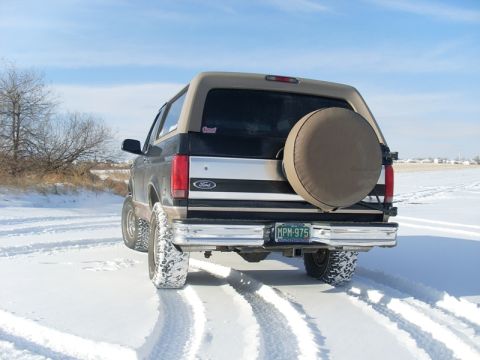 1996 Ford Bronco - A Ford Bronco drives through a snowy landscape, leaving tire tracks behind.