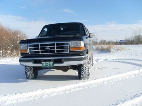 1996 Ford Bronco - A black Ford truck drives through the snow with its front end facing the camera.