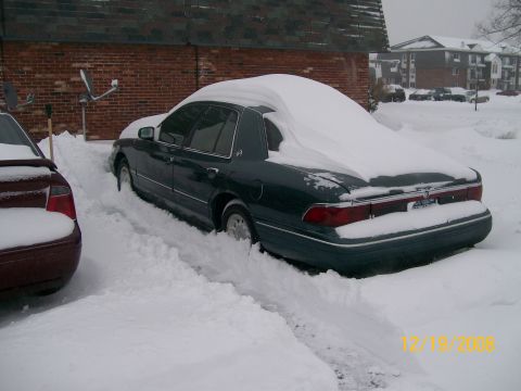 1995 Mercury Grand Marquis - A dark sedan is partially buried in snow, with another vehicle visible to its left.