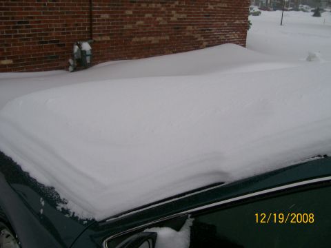 1995 Mercury Grand Marquis - A car is covered in snow next to a brick building during a winter storm.