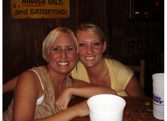 Two people smiling at a wooden bar table with white plastic cups