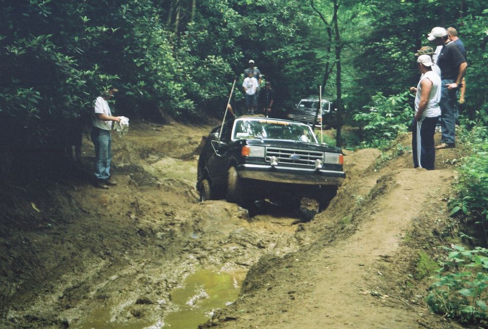 Black Ford F-Series truck navigating a muddy trail with people watching