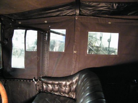 1915 Ford Model T - The interior of a vintage automobile features tufted leather seating and a canvas roof with small windows.