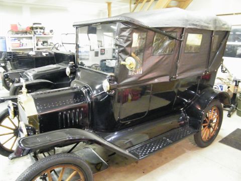 1915 Ford Model T - A black 1915 Ford Model T touring car is parked in a garage next to another similar vehicle.