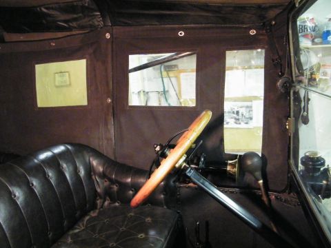 1915 Ford Model T - The interior of a 1915 Ford Model T features dark tufted leather seats and a prominent wooden steering wheel.