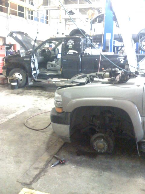 1992 Ford Bronco - Two trucks are in a garage, one undergoing repairs with its hood and doors open.