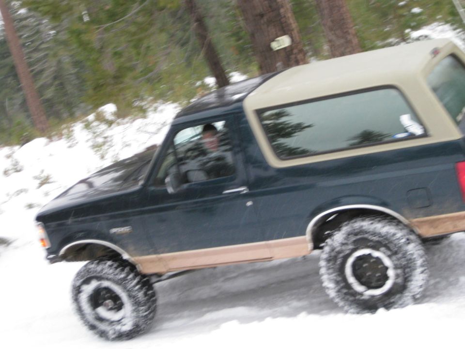 1995 Ford Bronco driving on a snowy road with trees in the background