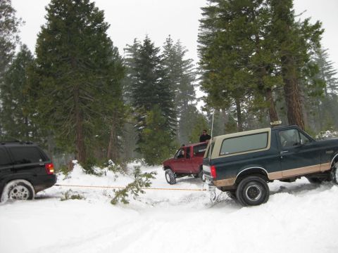1995 Ford Bronco - A dark green Bronco tows a black SUV through a snow-covered wooded area.