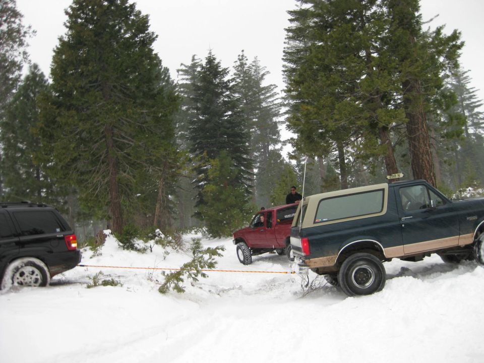 Black SUV being towed by a dark green Bronco in a snowy forest