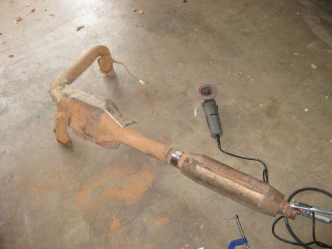 1995 Ford Bronco - Exhaust pipe and catalytic converter assembly, with a grinder nearby, resting on a concrete surface.