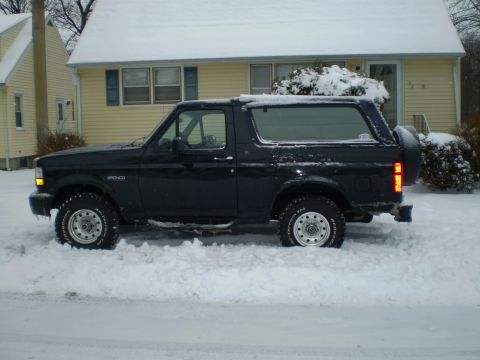 1996 Ford Bronco - A black 1996 Ford Bronco is partially buried in snow in front of a house.