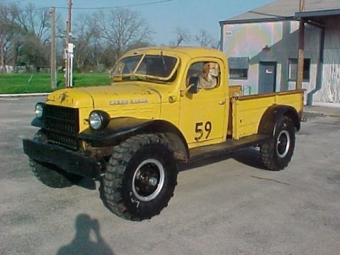 1991 Ford Bronco - A yellow pickup truck with a dog in the driver's seat is parked outside a building.